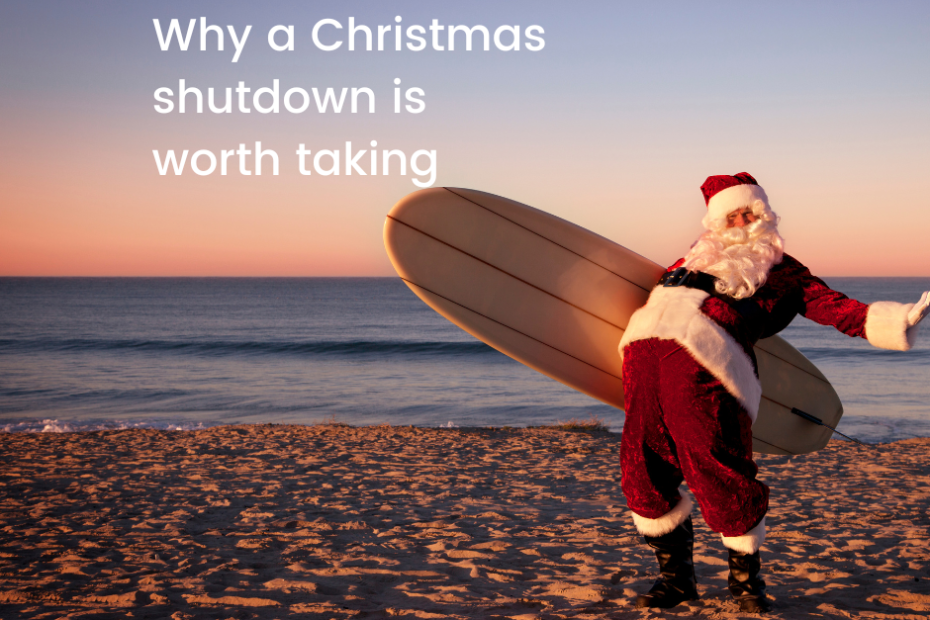 santa on a beach with a surfboard takling a well earned break and showing us why a christmas shutdown is worth taking
